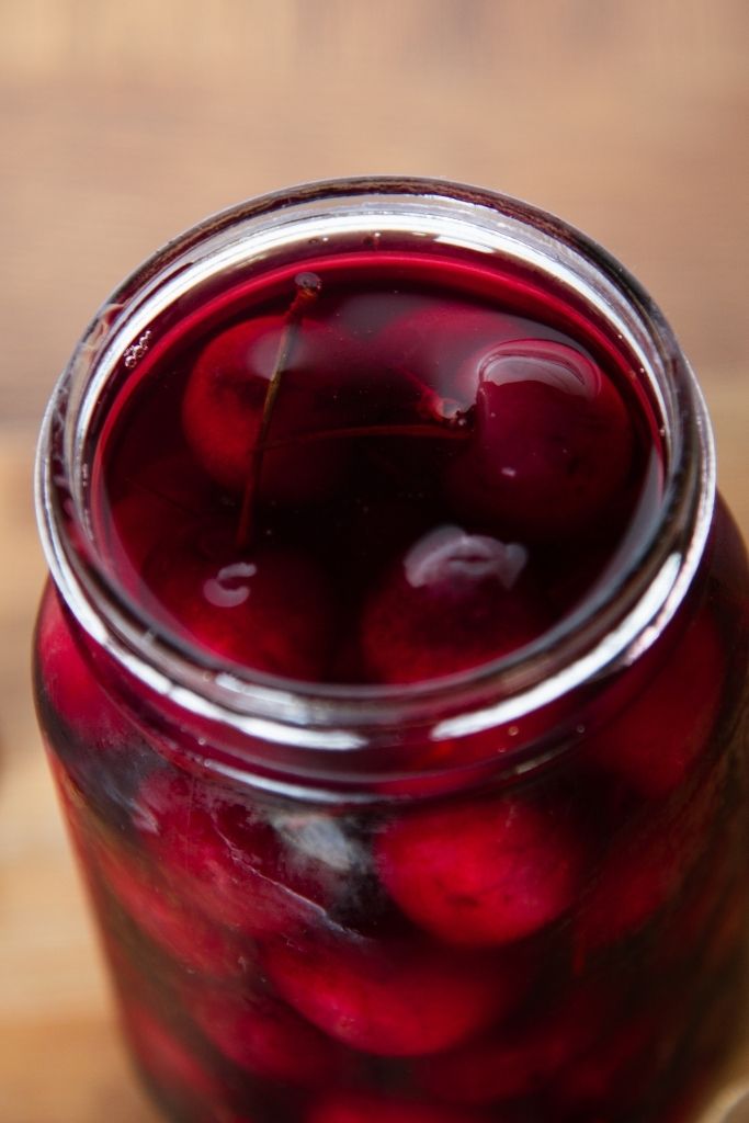 a close up of an open jar of pickled cherries 