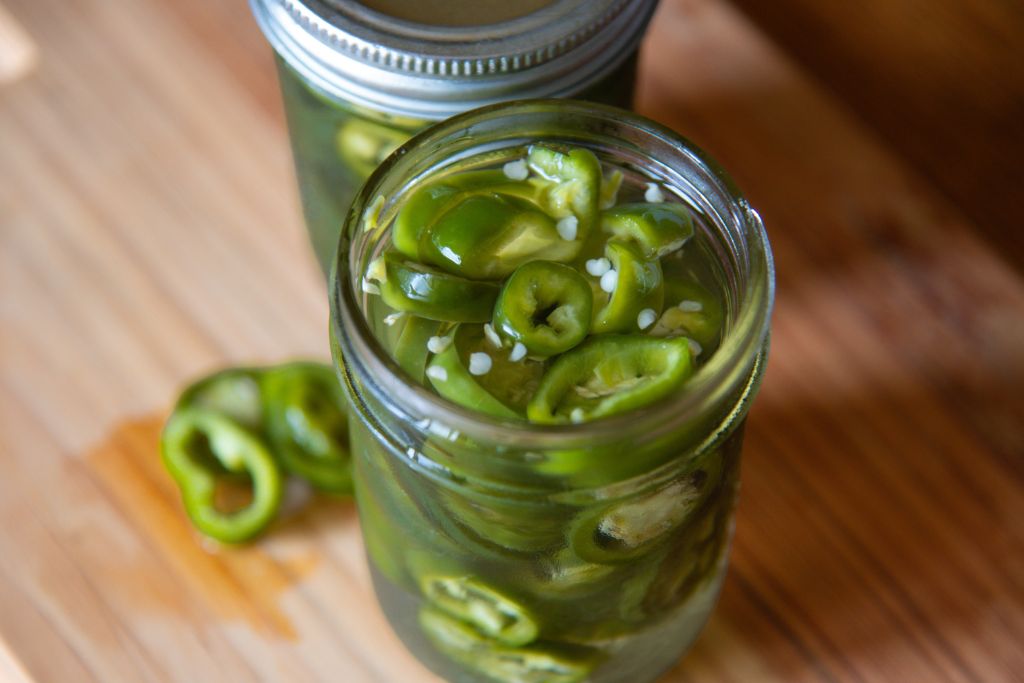 an open jar of pickled jalapenos, there is another jar and some jalapeno slices next to it