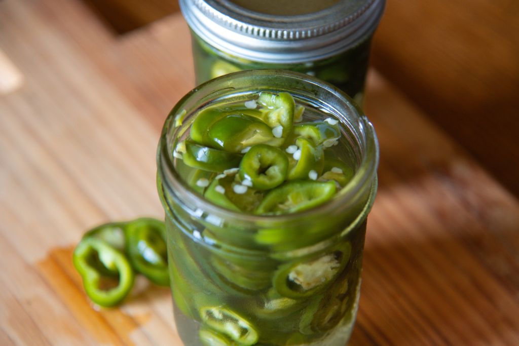 an open jar of pickled jalapenos with jalapeno slices next to it