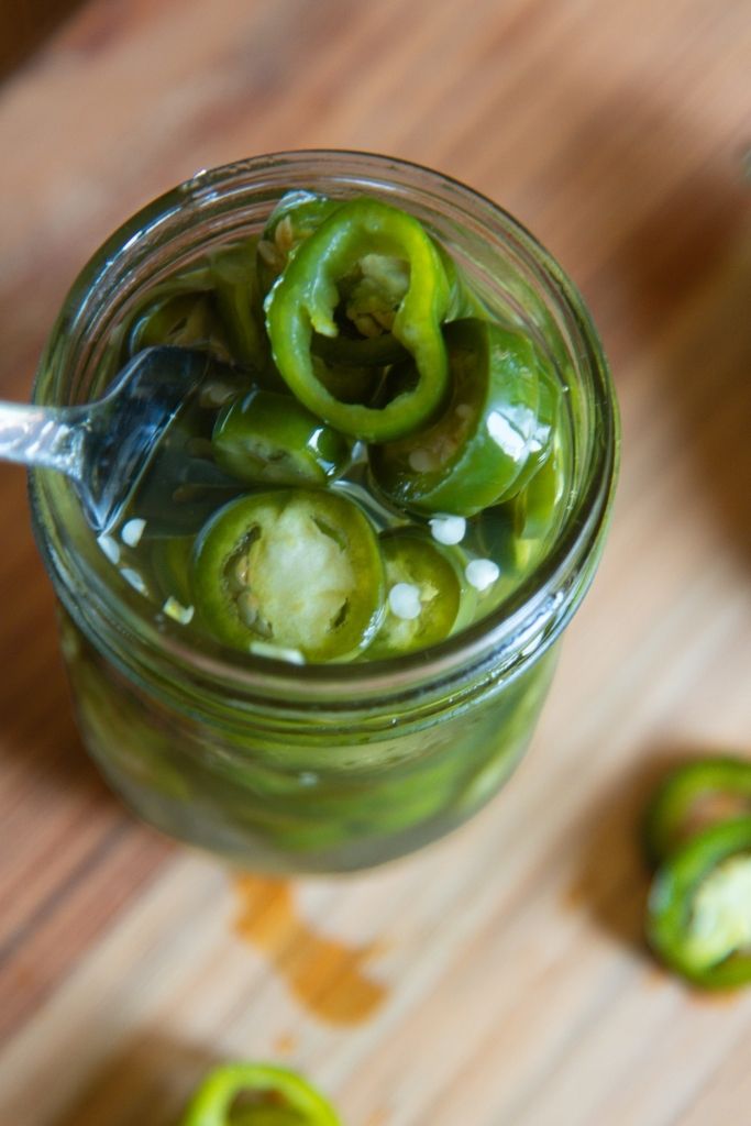 a close up of a jar of pickled jalapenos with a fork in it