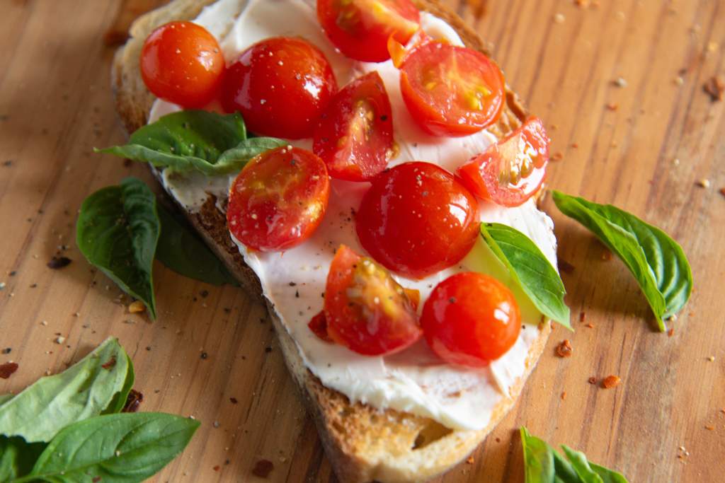 a close up of a piece of toast with pickled tomatoes on it and fresh basil next to it 