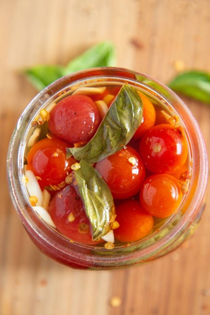 an open jar of pickled tomatoes with fresh basil next to it 