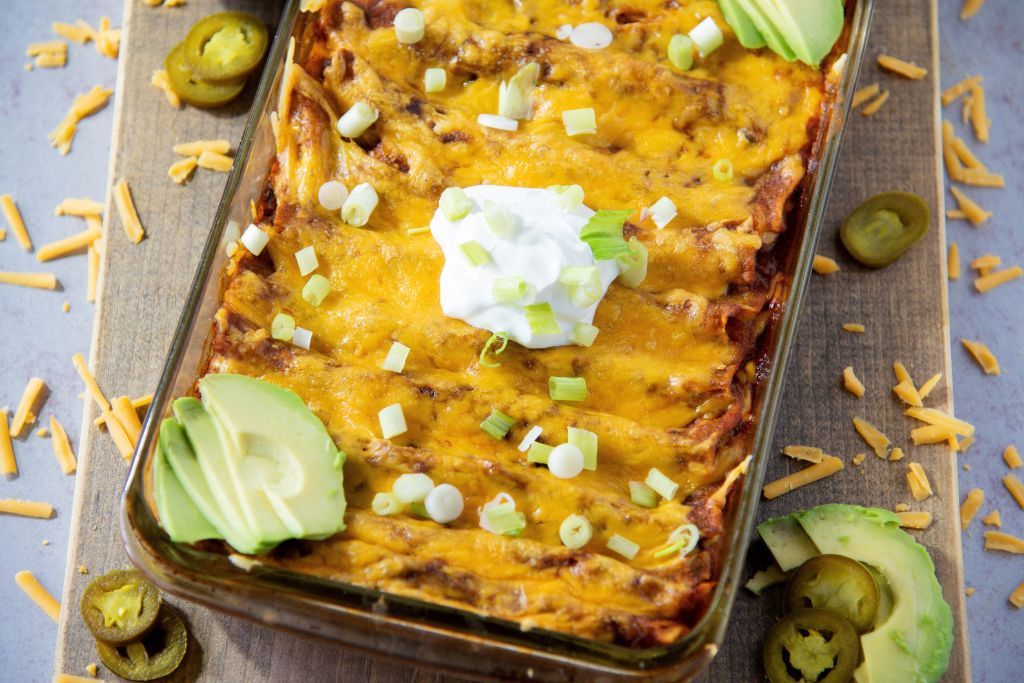 a pan of enchiladas with shredded cheese and pickled jalapenos around it