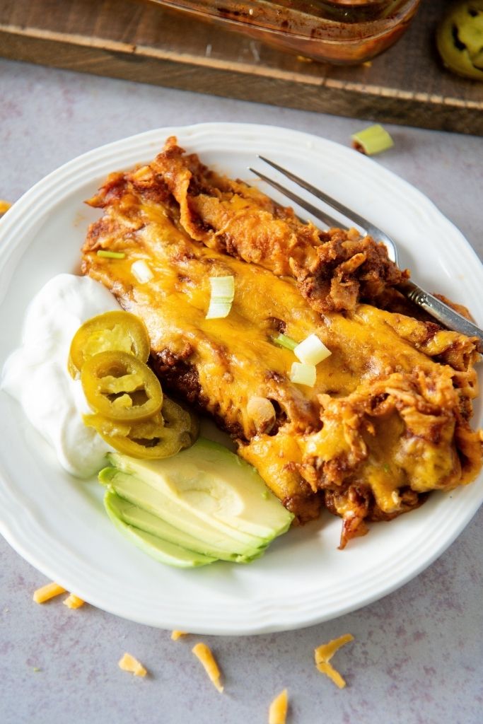 a close up of a plate of enchiladas with sour cream and avocado on the side