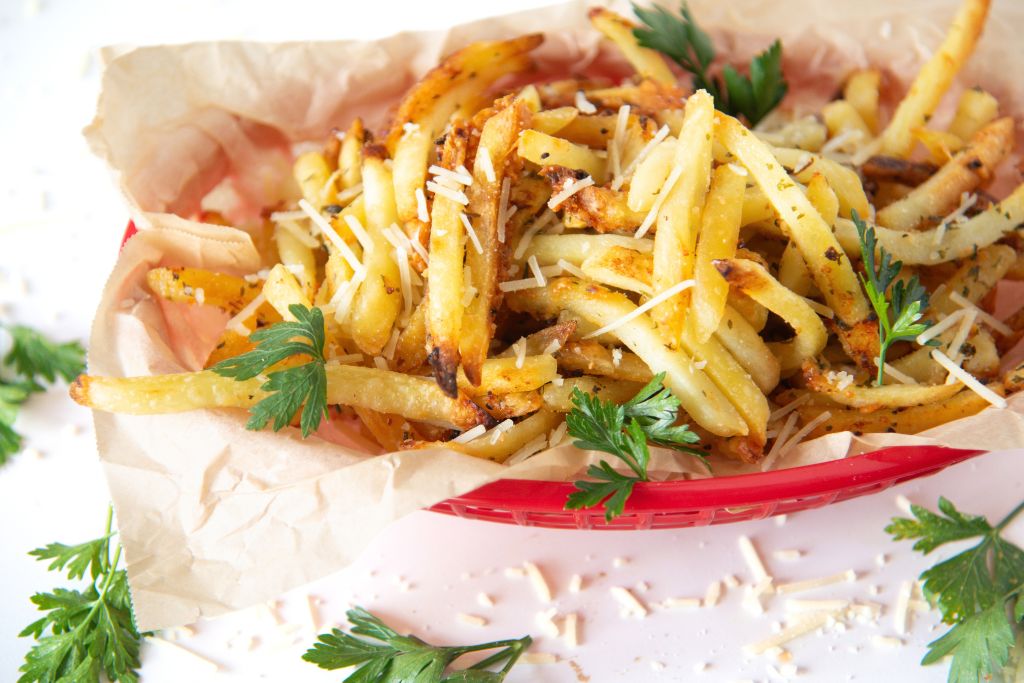 a basket of French fries with parsley and cheesed sprinkled over them and around the basket
