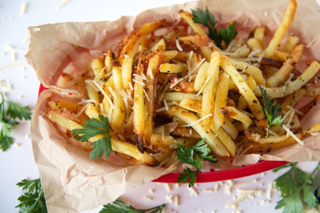 a basket of garlic fries with cheese and fresh parsley sprinkled around it