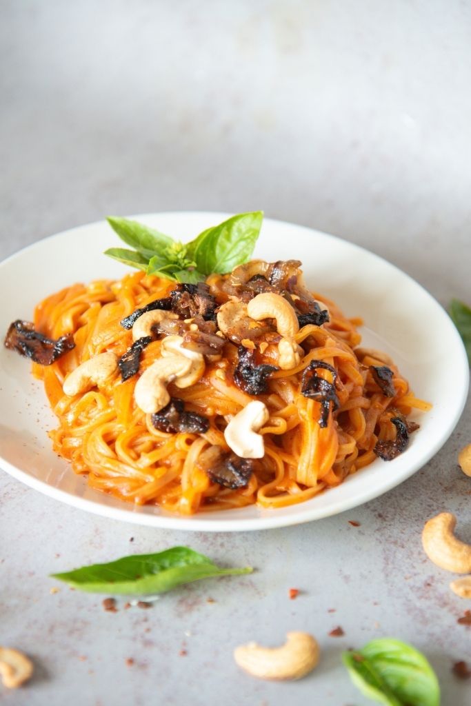 a plate of red curry noodles with shallots and cashews on top 