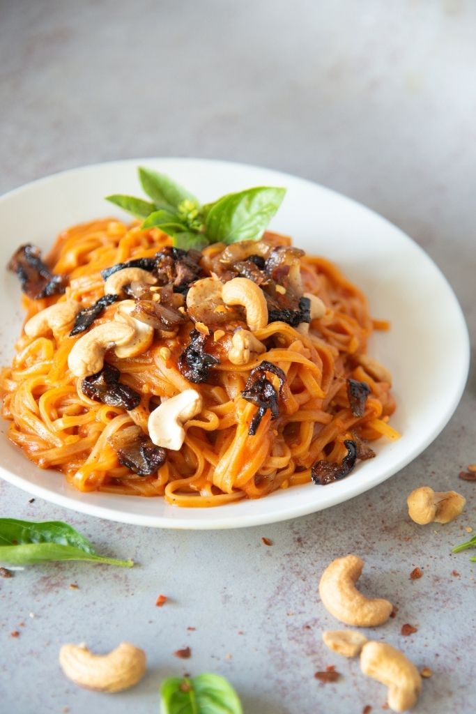 a plate of red curry noodles with basil and cashews in front of it 