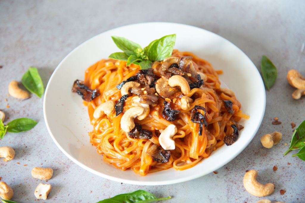 a plate of red curry noodles with fresh basil and cashews around it 