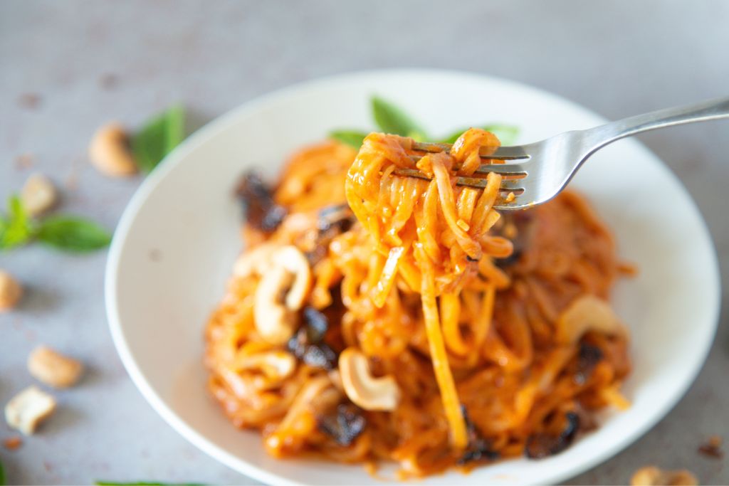 a forkful of noodles being held over a plate 